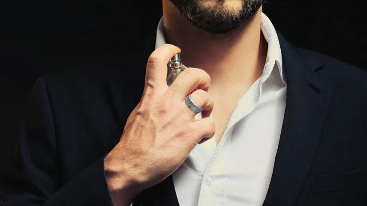 Man applying perfume to his neck against a dark background